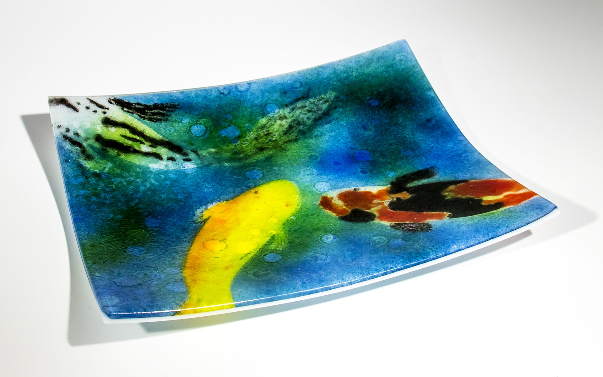 Advanced stenciling koi plate — fused powdered glass with a vibrant underwater scene featuring a yellow koi and a red-and-black koi on a blue-green background with lily pad accents. Private collection